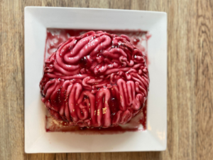 A pink and red Realistic Brain Cake on a white square plate placed on a table