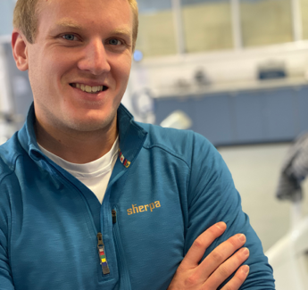 Blond man in blue, looing into camera, arms crossed